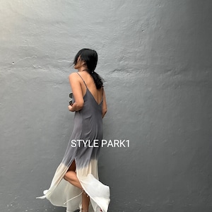 May include: A floor-length slip dress in a grey and white ombre design, featuring spaghetti straps and a high slit. The dress has the text "STYLE PARK1" on the side. The model is wearing gold strappy heels.