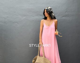 May include: A woman wearing a pink maxi dress with a ruffled hem and a straw tote bag. The text "STYLE PARK1" is visible on the wall behind her.