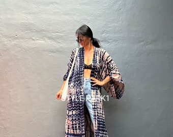 May include: A long, flowing tie-dye kimono in shades of blue and pink. The kimono has a relaxed fit and wide sleeves. The model is wearing the kimono over a black bra and blue jeans.