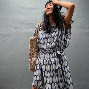 Könnte beinhalten: Ein dunkelblau-weißes Kleid mit Blattmuster, dazu ein passendes Stirnband und eine geflochtene Strohtasche. Das Kleid hat kurze Ärmel, einen V-Ausschnitt und einen Bindegürtel in der Taille. Der Text STYLE PARK1 ist auf dem Stoff zu sehen.