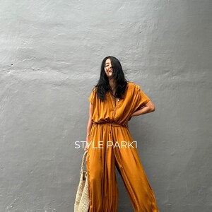 May include: A woman wearing a mustard yellow jumpsuit with a tie at the waist and a straw tote bag. The text "STYLE PARK1" is visible on the image.