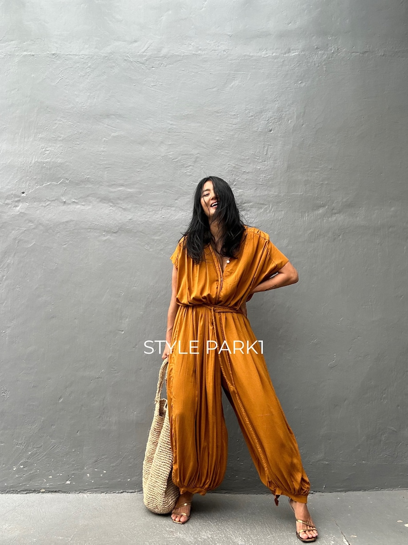 May include: A woman wearing a mustard yellow jumpsuit with a tie at the waist and a straw tote bag. The text "STYLE PARK1" is visible on the image.