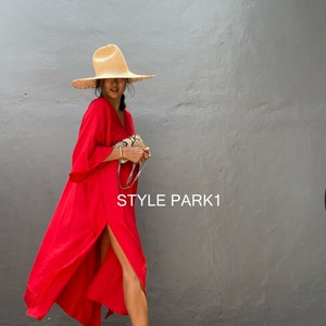 Puede incluir: Una mujer con un vestido rojo con una abertura alta, un sombrero de paja y tacones dorados. El vestido tiene mangas largas y cuello en V. Se sostiene un pequeño bolso con correa de cadena. El texto "STYLE PARK1" es visible.