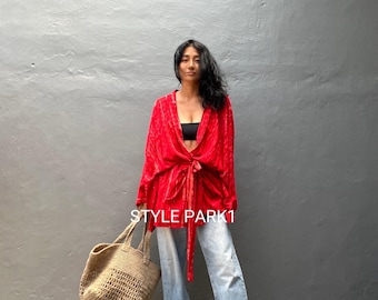May include: A woman wearing a red patterned shirt tied at the waist, light blue jeans, and a straw tote bag. The text "STYLE PARK1" is visible on the shirt.