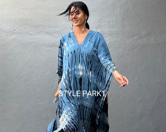 Op de afbeelding: Een vrouw draagt een blauwe en zwarte tie-dye kaftan met een V-hals. De kaftan heeft een lange, vloeiende silhouet en een zijsplit. De vrouw staat voor een grijze muur. De tekst "STYLE PARK1" is zichtbaar op de kaftan.