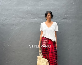 Könnte beinhalten: Eine Frau trägt ein weißes V-Ausschnitt-T-Shirt und eine rot-schwarz gefärbte Hose mit weitem Bein. Sie trägt eine gewebte beige Tragetasche. Der Text "STYLE PARK1" ist auf der Hose zu sehen.