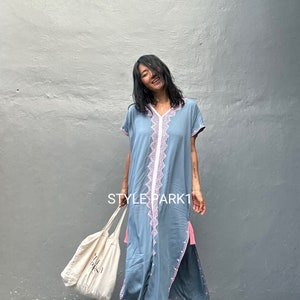 May include: A light blue maxi dress with pink and white embroidery. The dress has a V-neckline, short sleeves, and a side slit. The model is holding a white tote bag with the text "STYLEPARK1" printed on it.