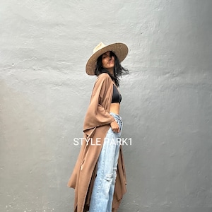 Può includere: Una donna indossa un kimono marrone con un cappello di paglia a tesa larga, jeans blu e sandali dorati. Il testo "STYLE PARK1" è visibile nell'immagine.