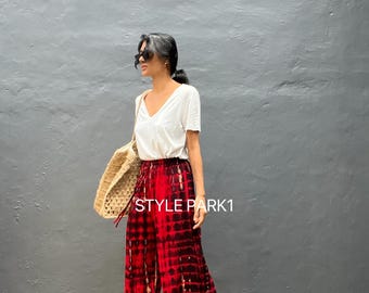 Könnte beinhalten: Weite Hose mit rotem und schwarzem Batikmuster. Das Outfit wird durch ein weißes V-Ausschnitt-Oberteil und eine Korbtasche ergänzt. Der Text "STYLE PARK1" ist auf der Hose zu sehen.