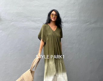 May include: A woman wearing a green and white ombre maxi dress with a v-neck and short sleeves. She is carrying a crocheted tote bag and wearing gold heeled sandals. The text "STYLE PARK1" is visible on the wall behind her.