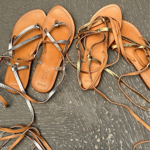May include: Two pairs of leather sandals with laces. One pair has silver laces and the other pair has gold laces.