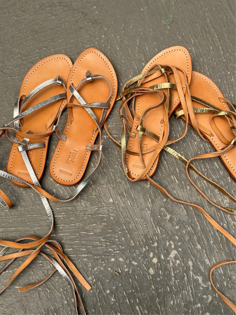 May include: Two pairs of leather sandals with laces. One pair has silver laces and the other pair has gold laces.