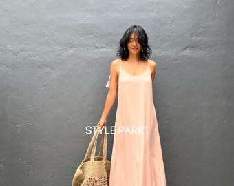 May include: A woman wearing a light pink maxi dress with a ruffled hem and a straw tote bag. The text "STYLE PARK1" is visible in the image.