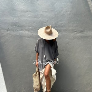 May include: A woman wearing a gray and white ombre maxi dress with a straw hat and sandals. She is carrying a woven tote bag. The text "STYLE PARK1" is visible on the dress.
