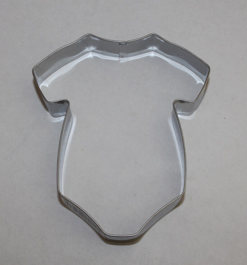 May include: A silver metal cookie cutter shaped like a baby onesie.