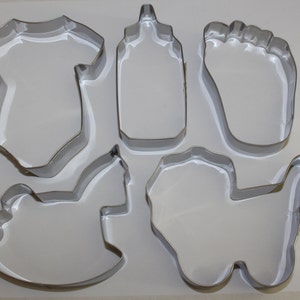 May include: Set of six metal cookie cutters in the shape of a baby bottle, a baby onesie, a baby foot, a rocking horse, a wagon, and a teddy bear.