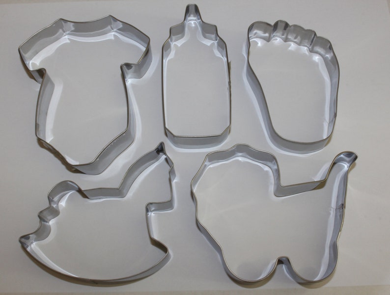 May include: Set of six metal cookie cutters in the shape of a baby bottle, a baby onesie, a baby foot, a rocking horse, a wagon, and a teddy bear.