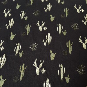 May include: Black fabric with a repeating pattern of white and green cactus silhouettes.