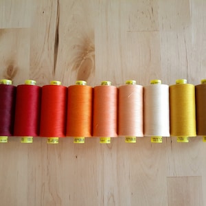 May include: A set of 10 spools of thread in shades of red, orange, yellow, and brown. The spools are arranged in a gradient from dark red to light brown.