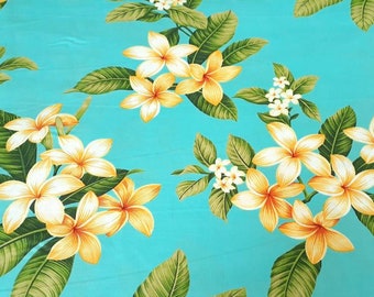 Op de afbeelding: Een turquoise stof met een herhalend patroon van witte en gele frangipani-bloemen en groene bladeren.