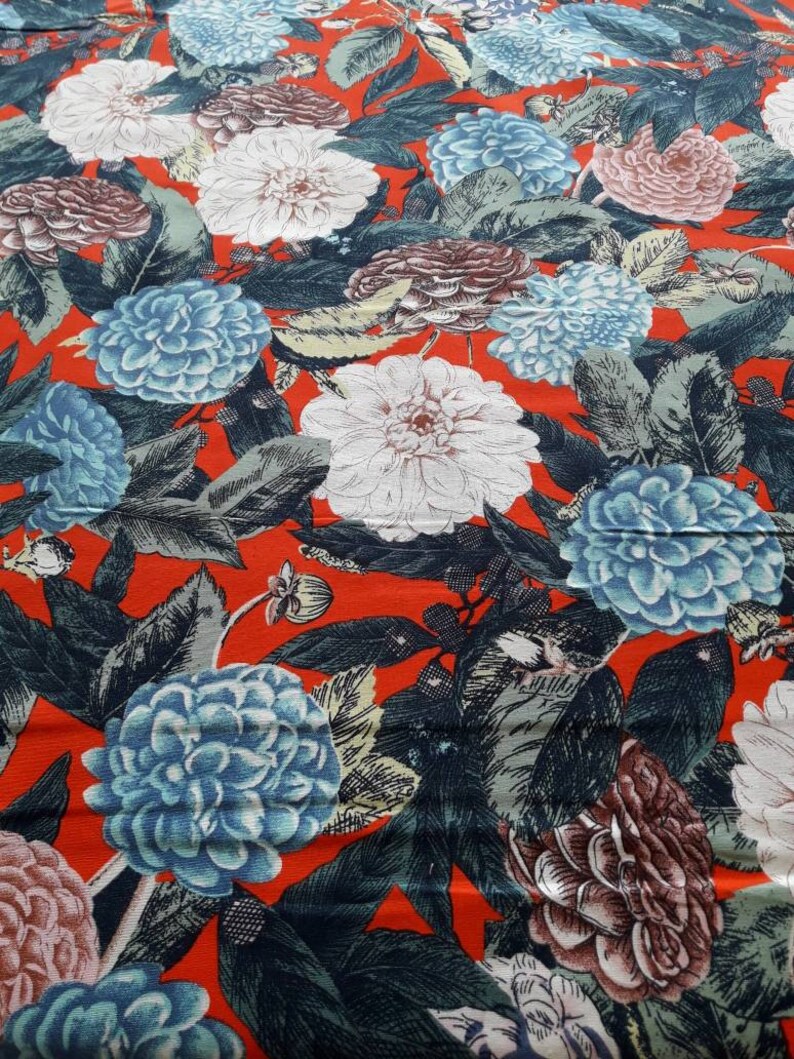 May include: Red fabric with a floral print featuring blue, white, and pink flowers. The flowers are stylized and have a vintage look.