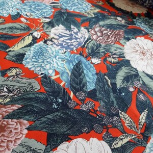 May include: Red fabric with a floral print featuring blue, white, and pink flowers with green leaves.