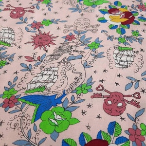 May include: Pink fabric with a repeating pattern of nautical and floral elements. The design includes ships, skulls with keys, suns, mermaids, and flowers in shades of blue, green, red, and yellow.