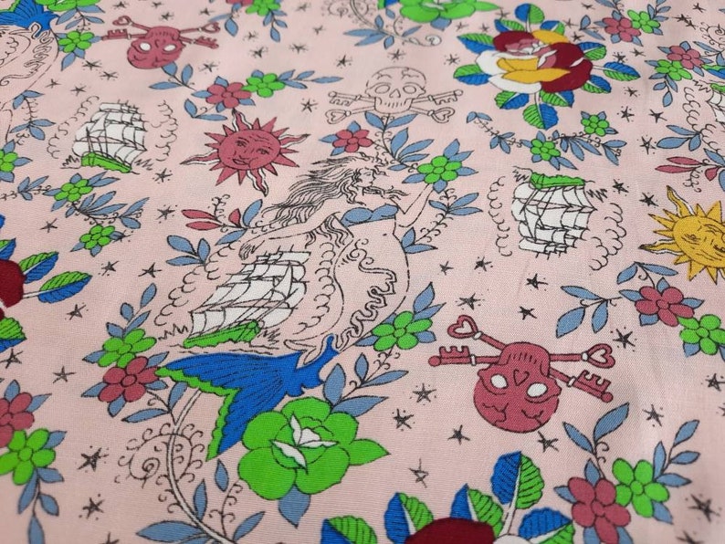 May include: Pink fabric with a repeating pattern of nautical and floral elements. The design includes ships, skulls with keys, suns, mermaids, and flowers in shades of blue, green, red, and yellow.