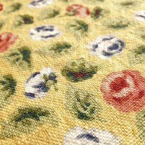 May include: Close-up of a yellow fabric with a repeating pattern of red, white, and blue flowers. The fabric has a textured surface.