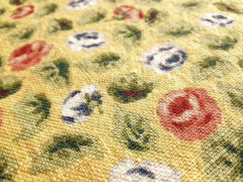 May include: Close-up of a yellow fabric with a repeating pattern of red, white, and blue flowers. The fabric has a textured surface.