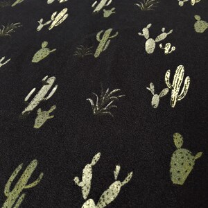 May include: Black fabric with a repeating pattern of green cactus silhouettes. The cactus silhouettes are in various shapes and sizes.
