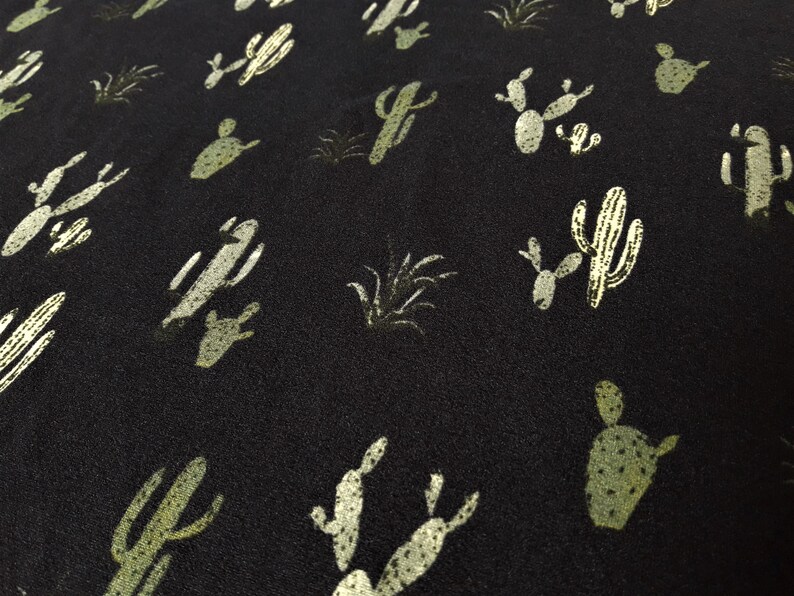 May include: Black fabric with a repeating pattern of green cactus silhouettes. The cactus silhouettes are in various shapes and sizes.