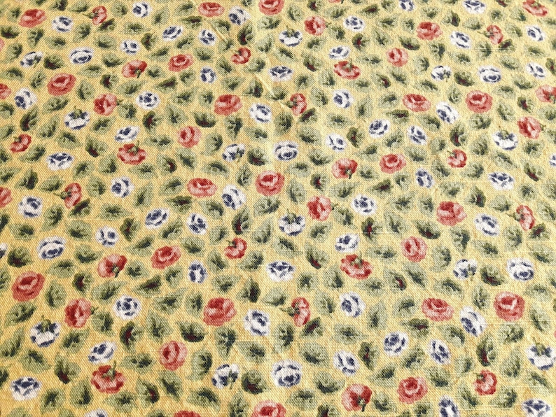 May include: A yellow fabric with a repeating pattern of red, white, and blue flowers. The flowers are small and delicate, and the fabric has a slightly textured surface.