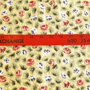 May include: Yellow fabric with a repeating pattern of small red, white, and blue flowers. A red ruler with the text "AL EXCHANGE 600 35th Ave." is placed across the fabric.