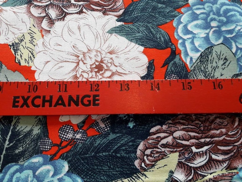 May include: Red fabric with a floral print featuring white, blue, and brown flowers. A red ruler with the word "EXCHANGE" printed on it is placed across the fabric. The ruler measures 10 to 16 inches.