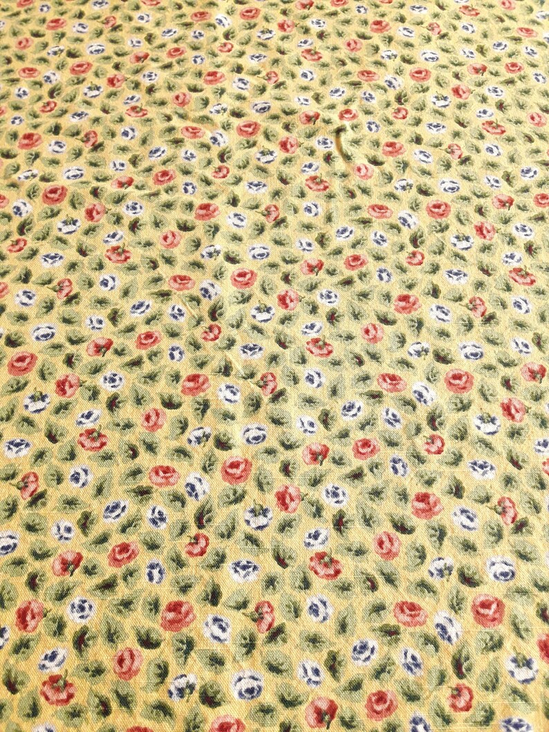 May include: Yellow fabric with a repeating pattern of small red and white flowers with green leaves.
