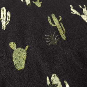 May include: Black fabric with a repeating pattern of green cactus plants.
