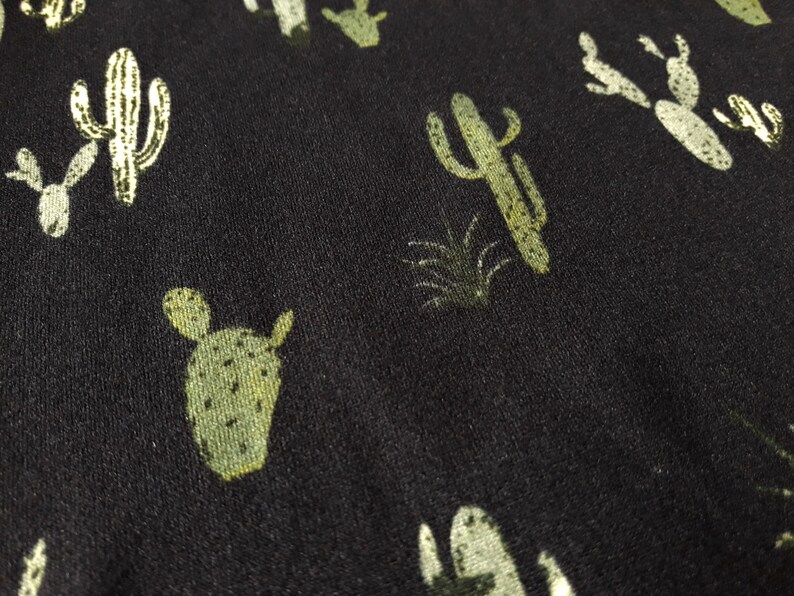 May include: Black fabric with a repeating pattern of green cactus plants.
