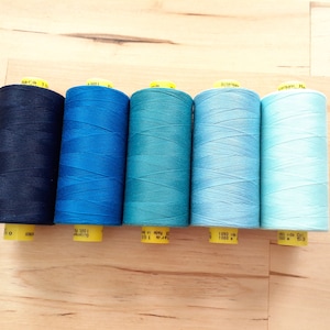 May include: Six spools of thread in various shades of blue, from dark navy to light blue. Each spool has a yellow label with the brand name and yardage.