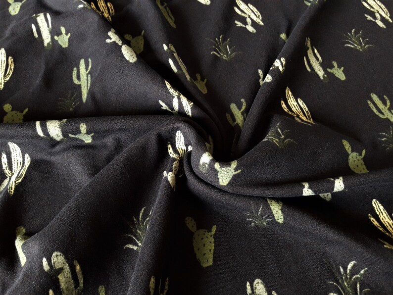 May include: Black fabric with a repeating pattern of green and yellow cacti and plants.