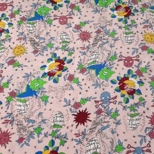 May include: Pink fabric with a repeating pattern of traditional tattoo imagery. The design includes roses, swallows, ships, skulls, keys, suns, and stars in red, yellow, green, blue, and black.