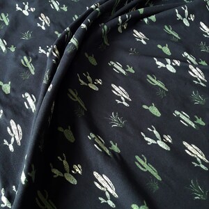 May include: Black fabric with a repeating pattern of green cacti. The fabric is folded and draped.