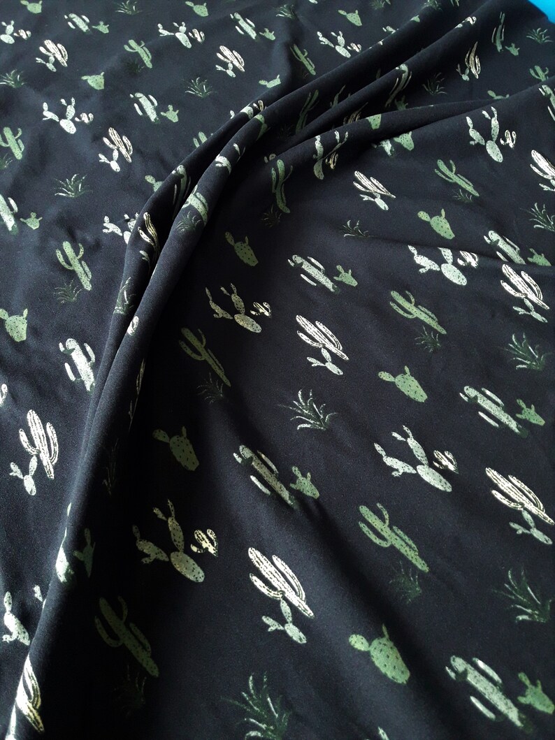 May include: Black fabric with a repeating pattern of green cacti. The fabric is folded and draped.