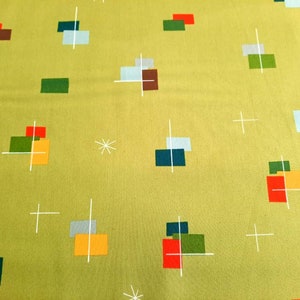 May include: A yellow fabric with a geometric pattern of white lines, red, green, blue, and orange squares. The pattern is reminiscent of mid-century modern design.