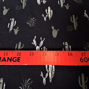 May include: Black fabric with a white cactus print. The fabric is measured with a red ruler that reads "EXCHANGE" and "600 35".