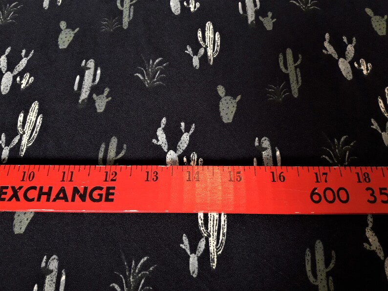 May include: Black fabric with a white cactus print. The fabric is measured with a red ruler that reads "EXCHANGE" and "600 35".