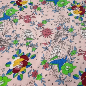 May include: Pink fabric with a repeating pattern of nautical and floral elements. The design includes sailing ships, roses, skulls with crossed bones, suns, and mermaids, in shades of red, yellow, blue, and green.