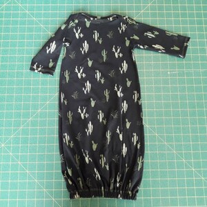May include: A black baby gown with a white cactus print. The gown has long sleeves and a gathered bottom.