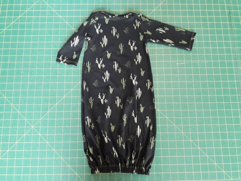 May include: A black baby gown with a white cactus print. The gown has long sleeves and a gathered bottom.