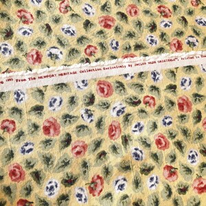 May include: Yellow fabric with a floral pattern of red, white, and blue flowers. The fabric has a white label with the text "1991 From The NEWPORT HERITAGE Collection Exclusively by JACKIE NASH ORIGINALS. Printed in the U.S.A."
